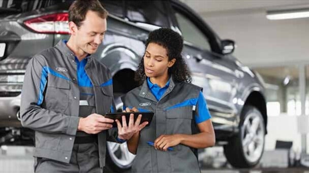 Woman smiling in driver's seat while sales person explains car features.